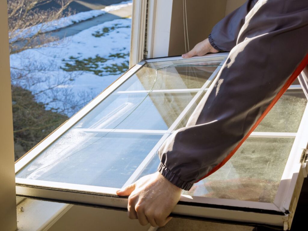 Worker removing an old window panel from inside a home in winter