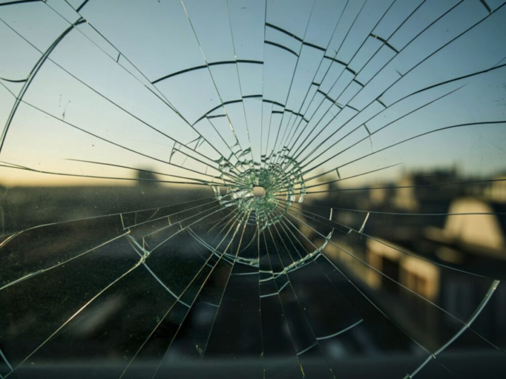 Shattered window glass with impact point and spiderweb cracks