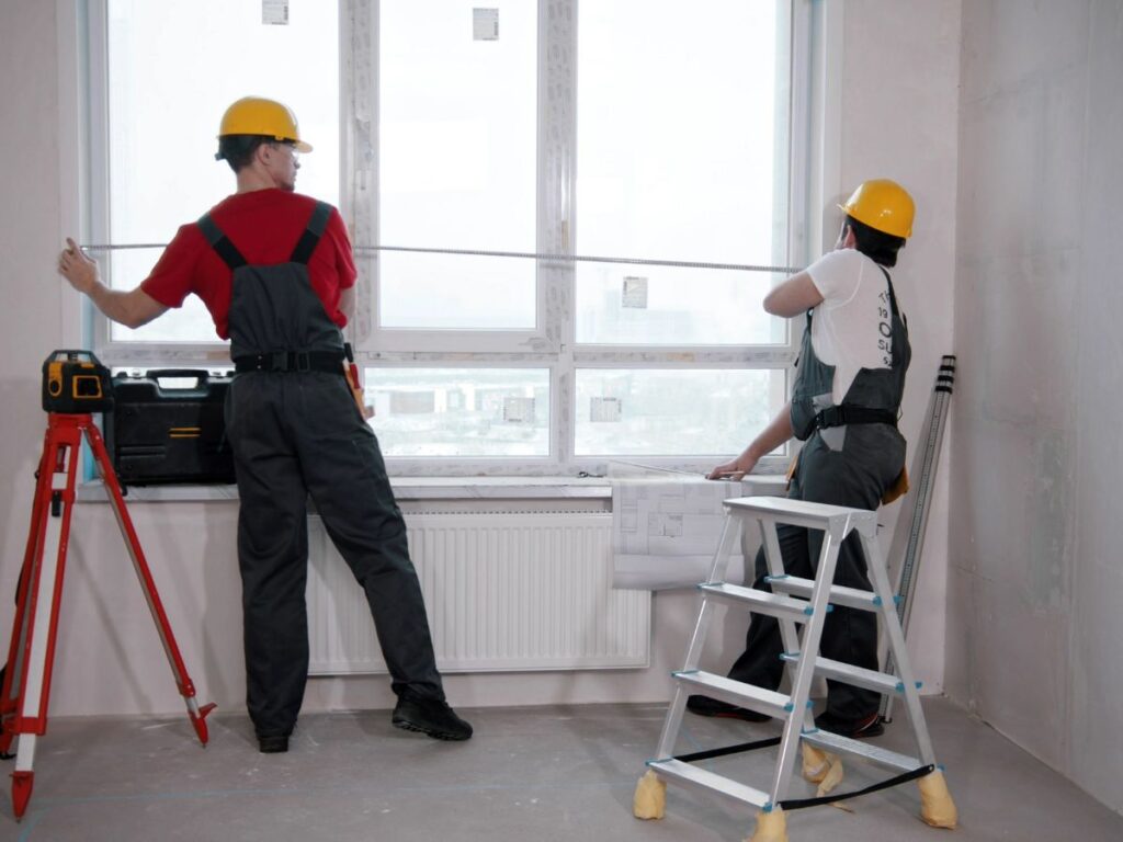 Two installers measuring a window opening during replacement work